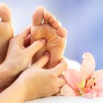 Macro close up of hands massaging female foot. Feet next to flower and candle against colourful background.